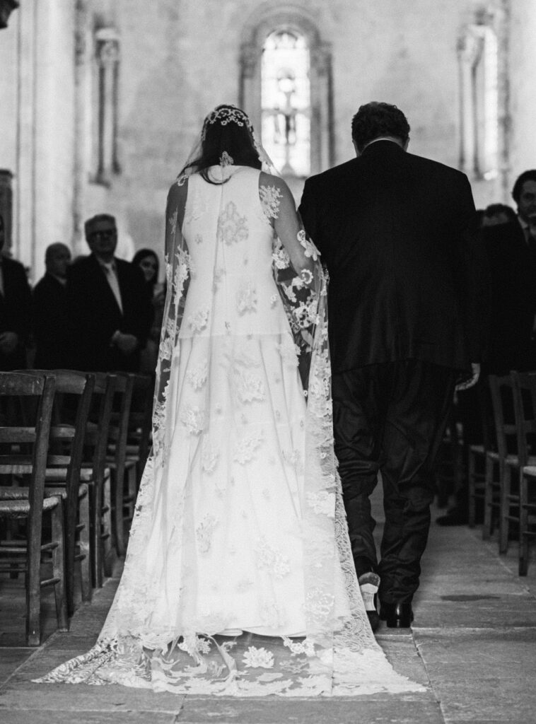 Mariée entrant dans une église portant un voile en dentelle brodée